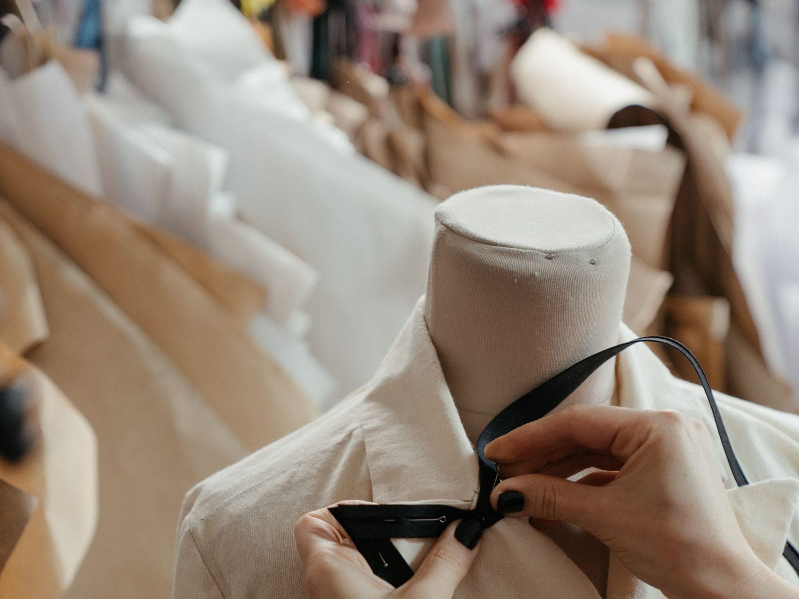 Hands pinning trim onto a garment fitted to a dress form during sample review