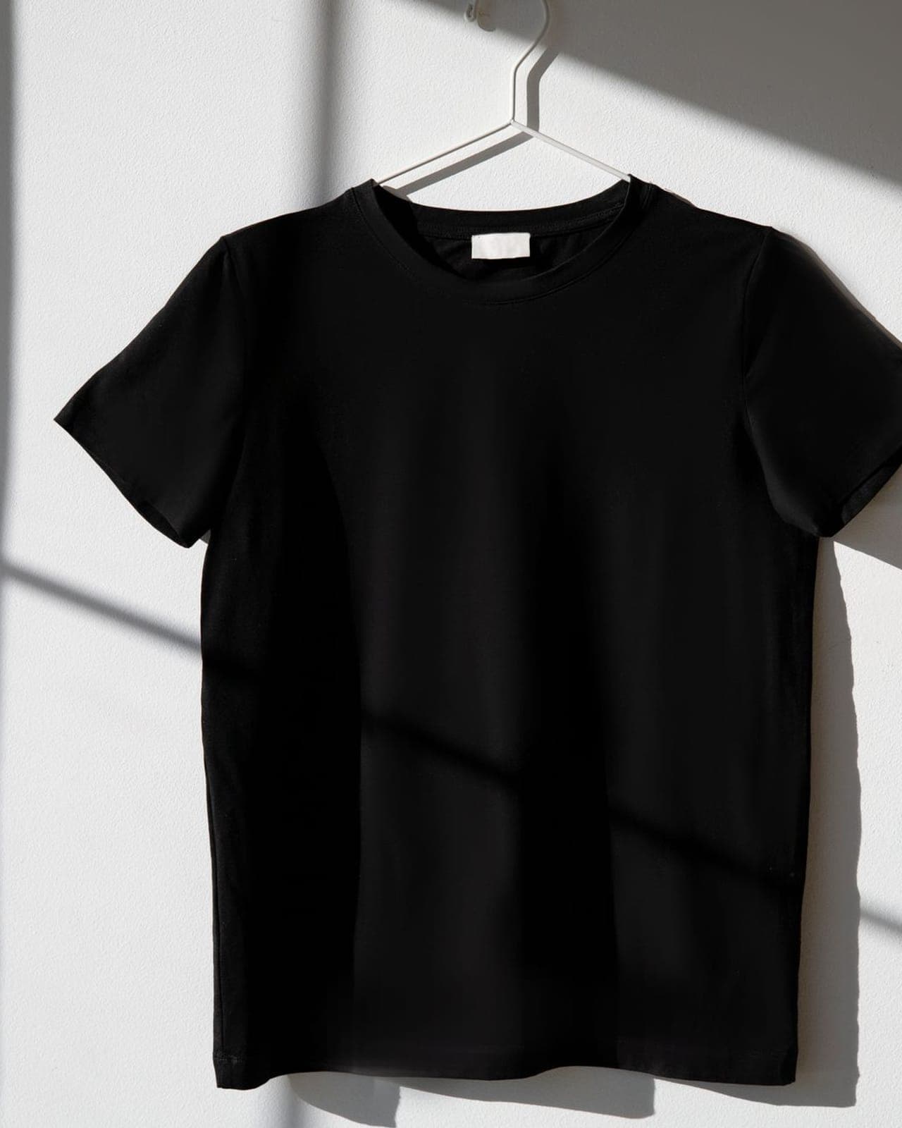 Plain black knitted garment on a hanger against a white wall, lit to show the shoulder seam and hem