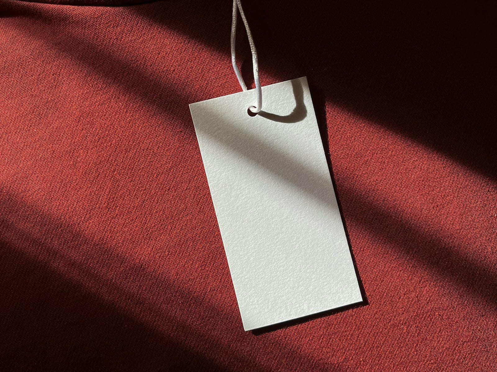 Blank hang tag on a string attached to a deep red knitted garment, ready for brand artwork