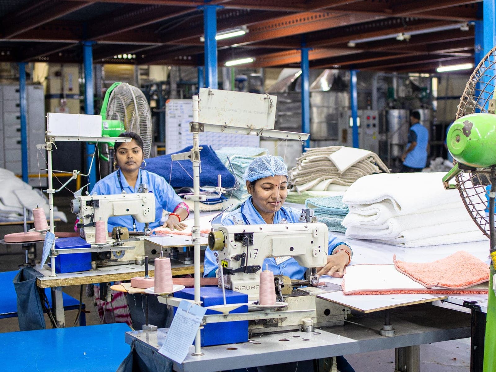 Garment production floor with sewing operators working beside stacks of folded knitwear